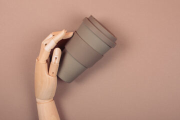 Wooden hand holding reusable cup of coffee