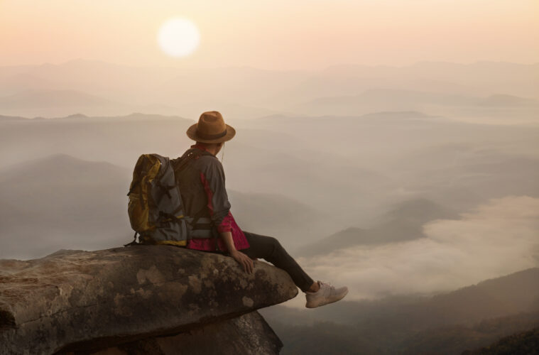 Backpacker man sitting on cliff with sunset background