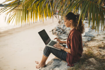 Woman sitting with laptop on the summer beach at sunset