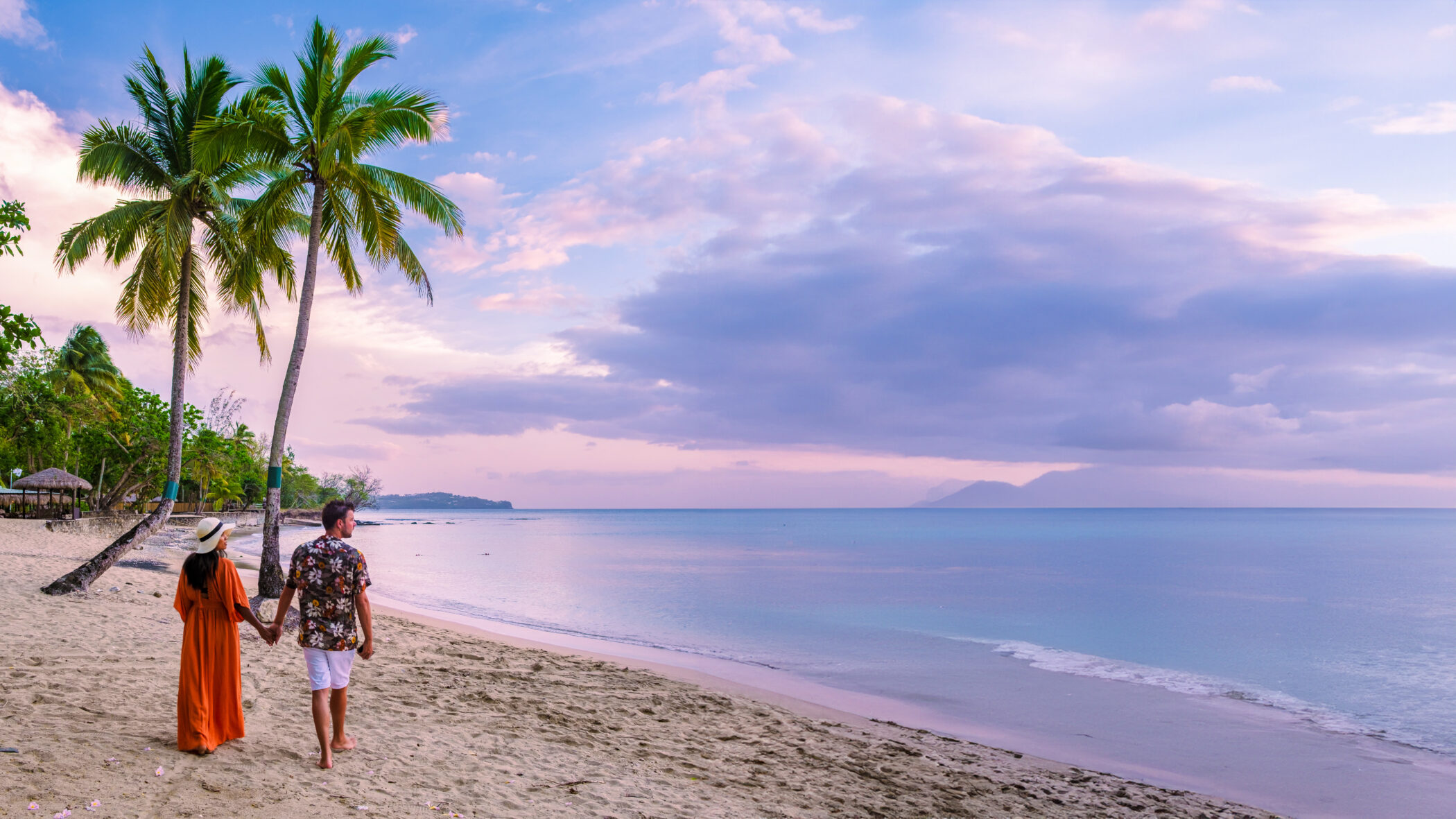 Two adults walking along the beach at sunset in St Lucia with palm trees in the background.
