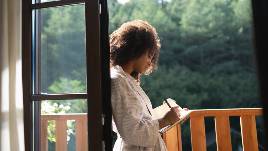 woman at hotel window writes in journal in the sun